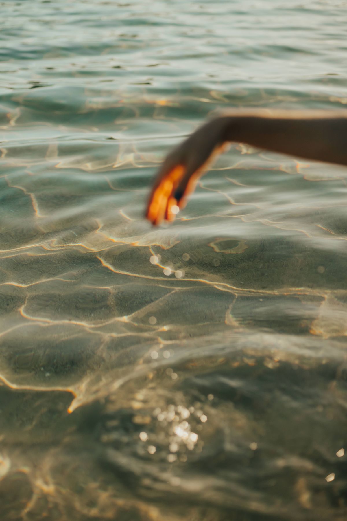 A hand trailing through sunlit water