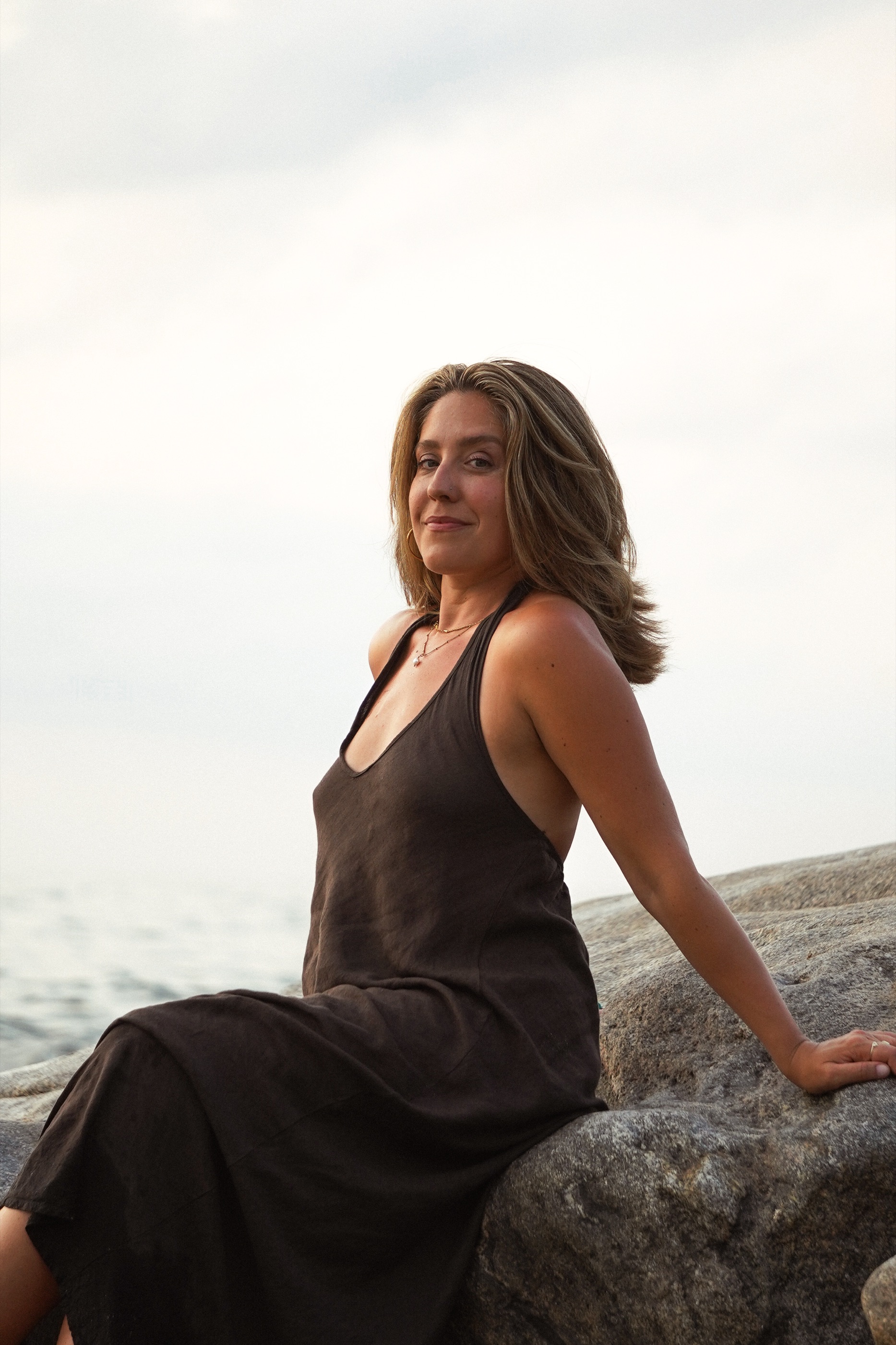 Niki Wells seated on seaside rocks in a black dress