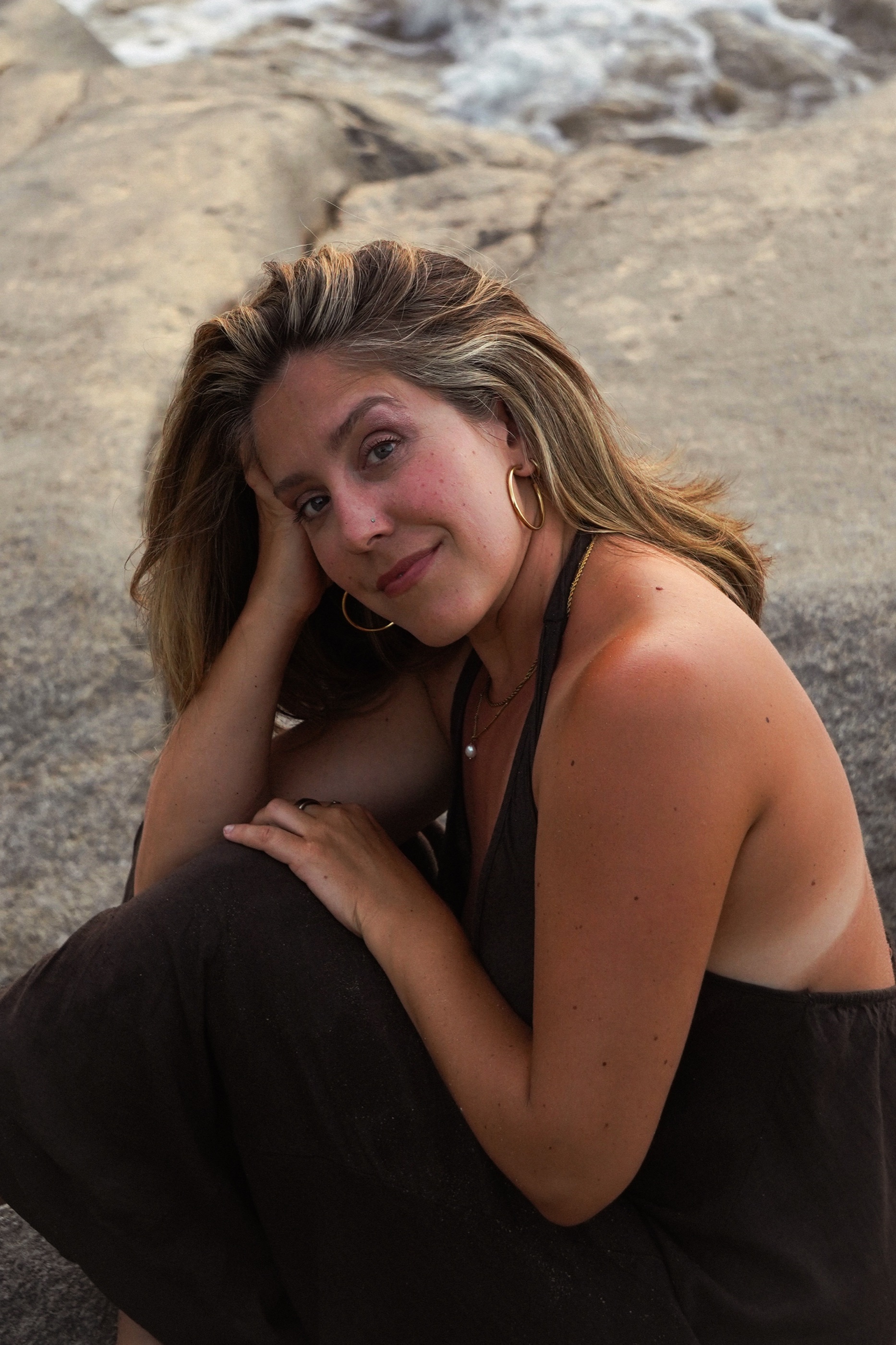 A close portrait of Niki seated on seaside rocks