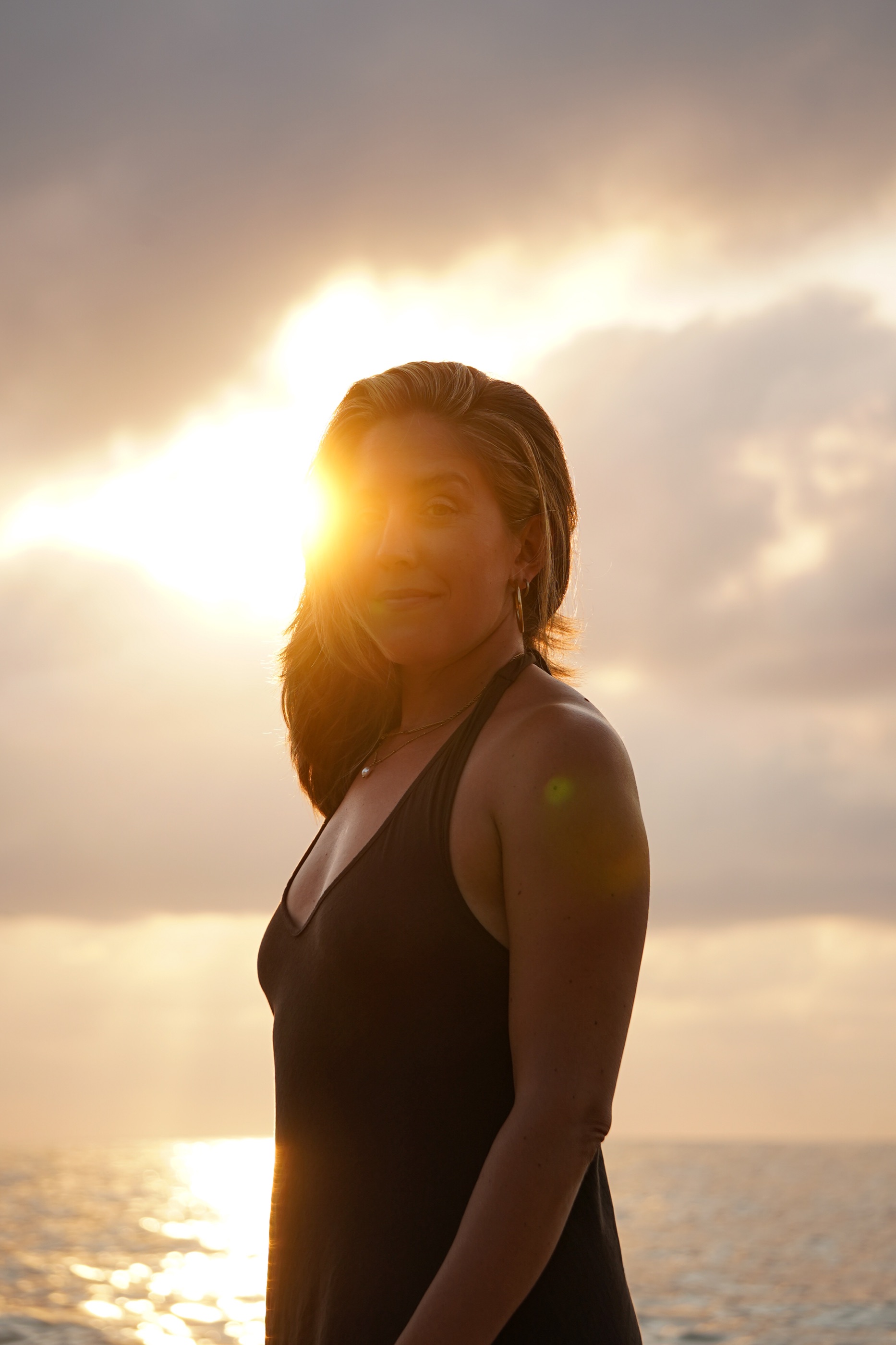 Niki standing in golden sun beside the ocean